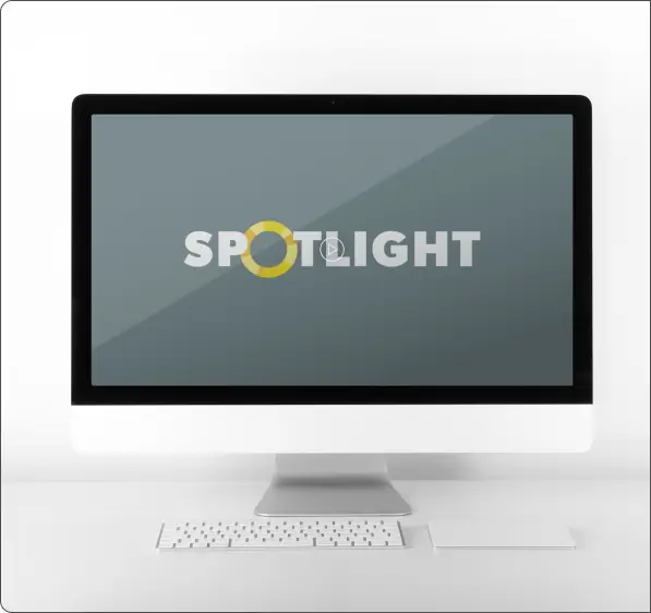 Front-facing desktop computer on a white background showing the Spotlight logo centered on the screen, with a keyboard and trackpad placed neatly below.